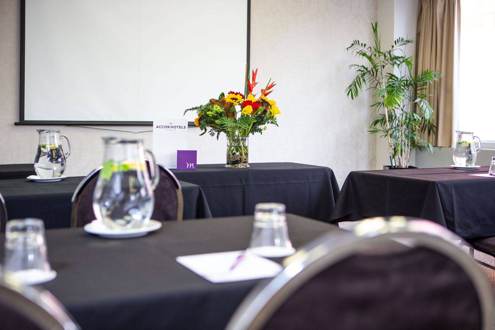 Interiors of the Abel Tasman Meeting Room with small tables with chairs facing a projector screen on the wall